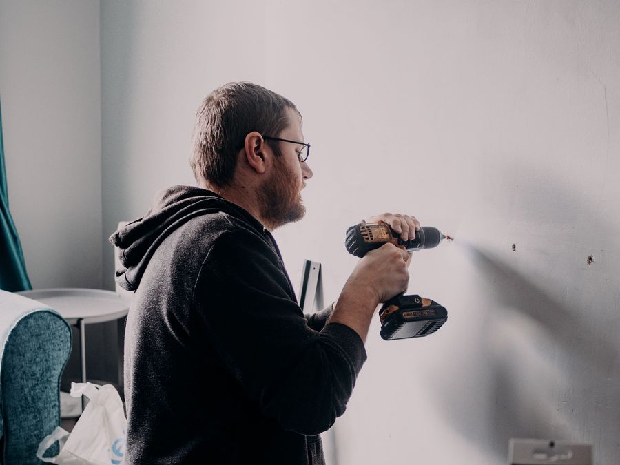 Homme perçant un mur intérieur à la perceuse pour installer une fixation.