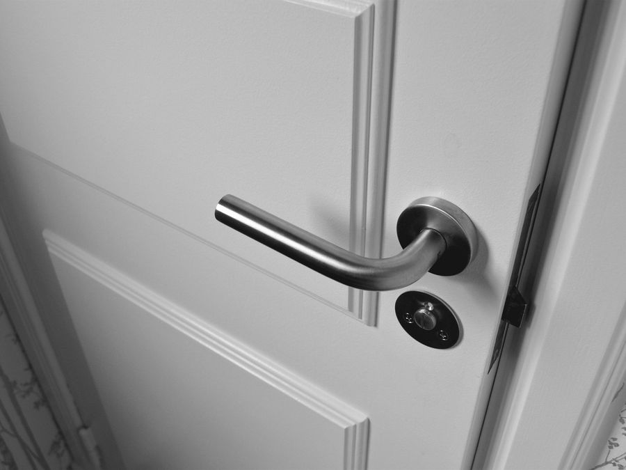 Poignée et serrure en inox sur une porte intérieure blanche.